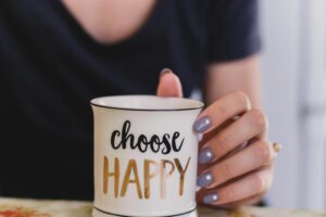 A woman holds a mug with 'choose happy' text indoors, promoting positivity.